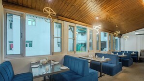 A restaurant with blue booths and tables, wooden ceiling, and large windows. - Hotel Riviera By Mount view (Anantnag)