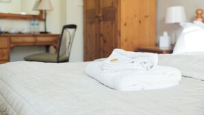 A neatly made bed with folded white towels and a wooden wardrobe in the background. - The Vestry (Chichester)