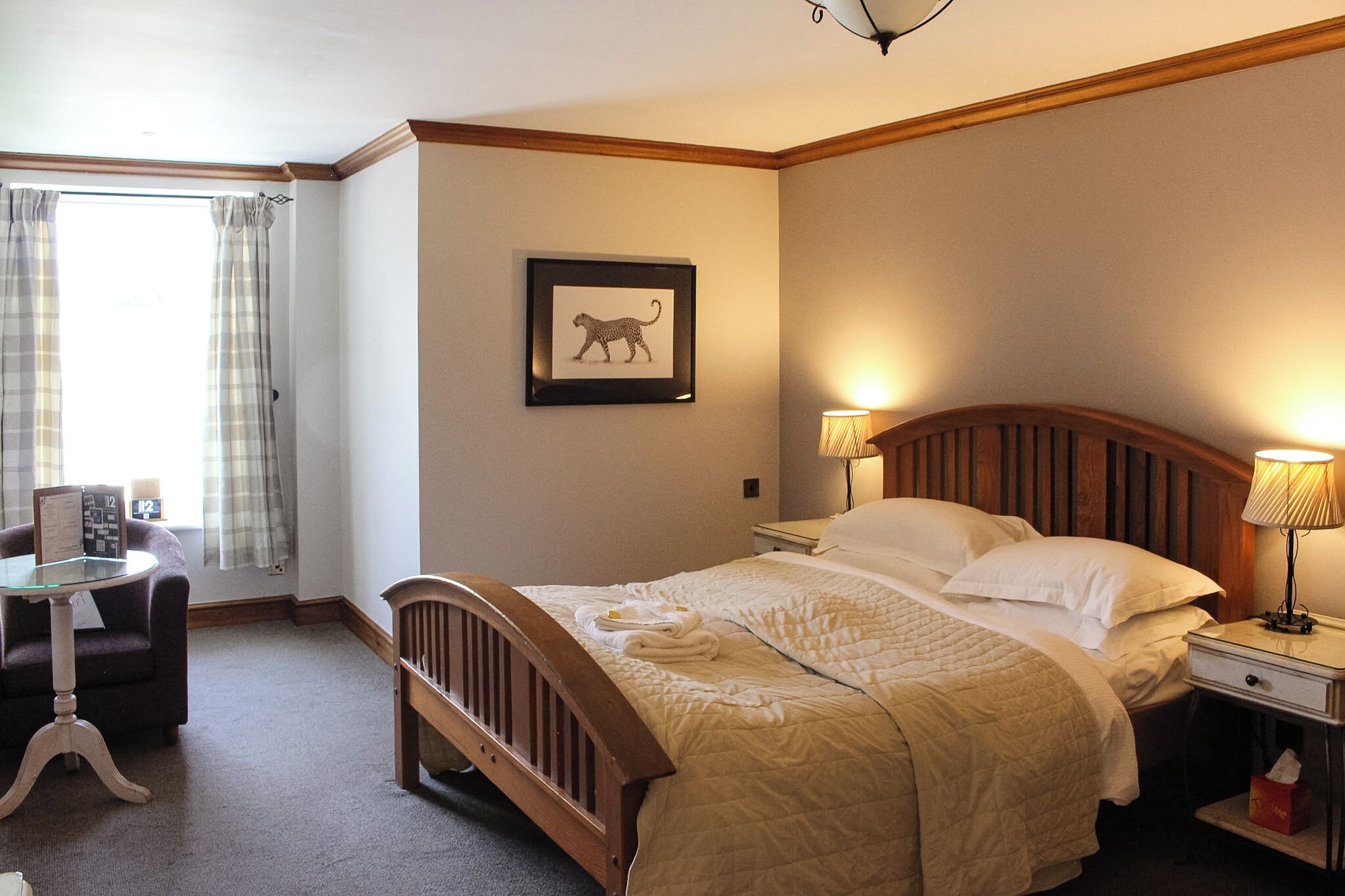 A hotel room with a bed, bedside lamps, a chair, a desk, and a framed picture on the wall.
