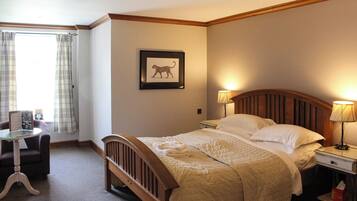 A hotel room with a bed, bedside lamps, a chair, a desk, and a framed picture on the wall.