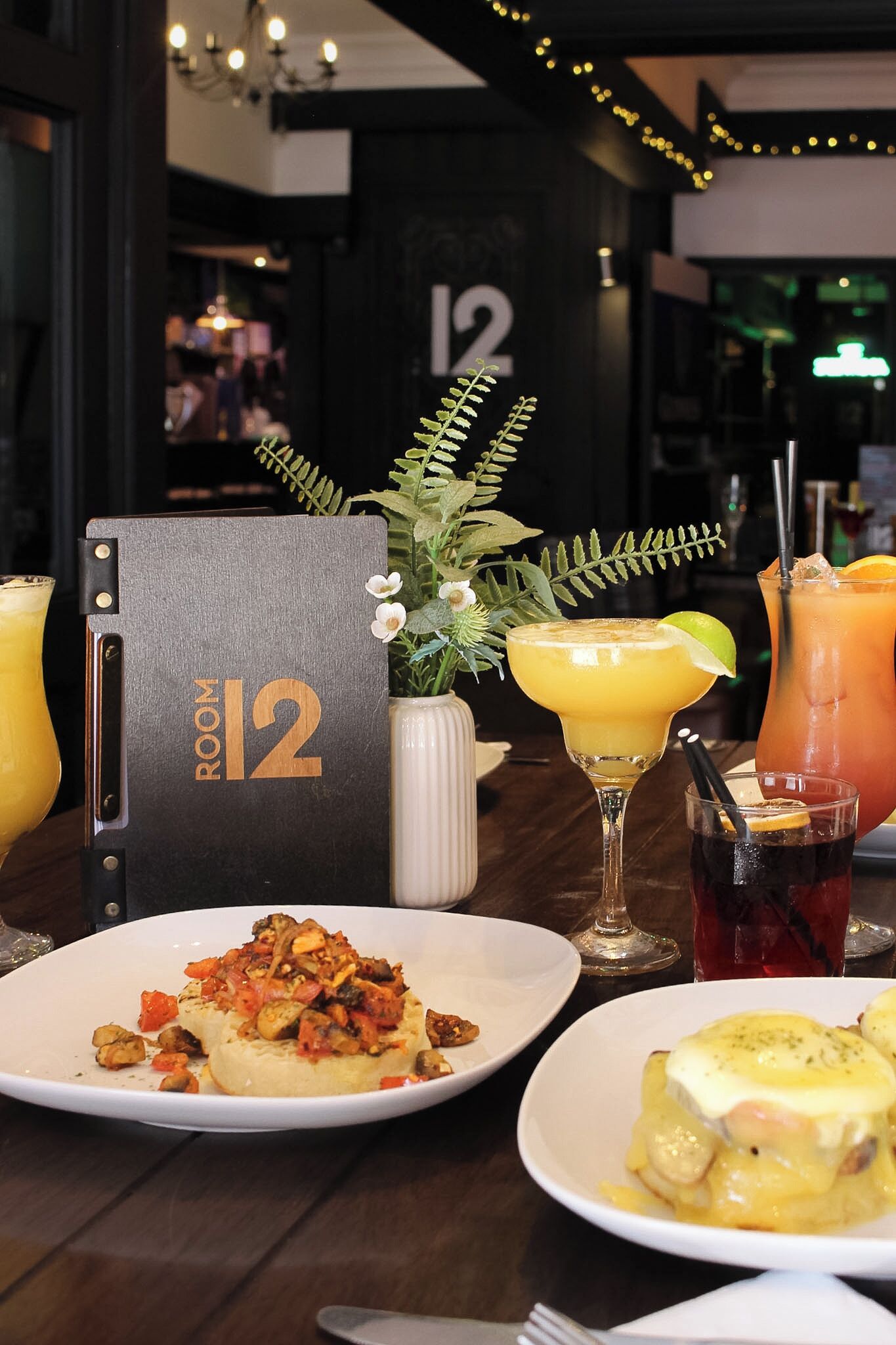 A table set with a number 12 sign, two plates of food, and two drinks.
