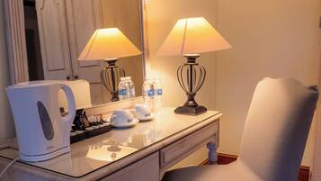 A room with a vanity, two lamps, a chair, a mirror, and a kettle.