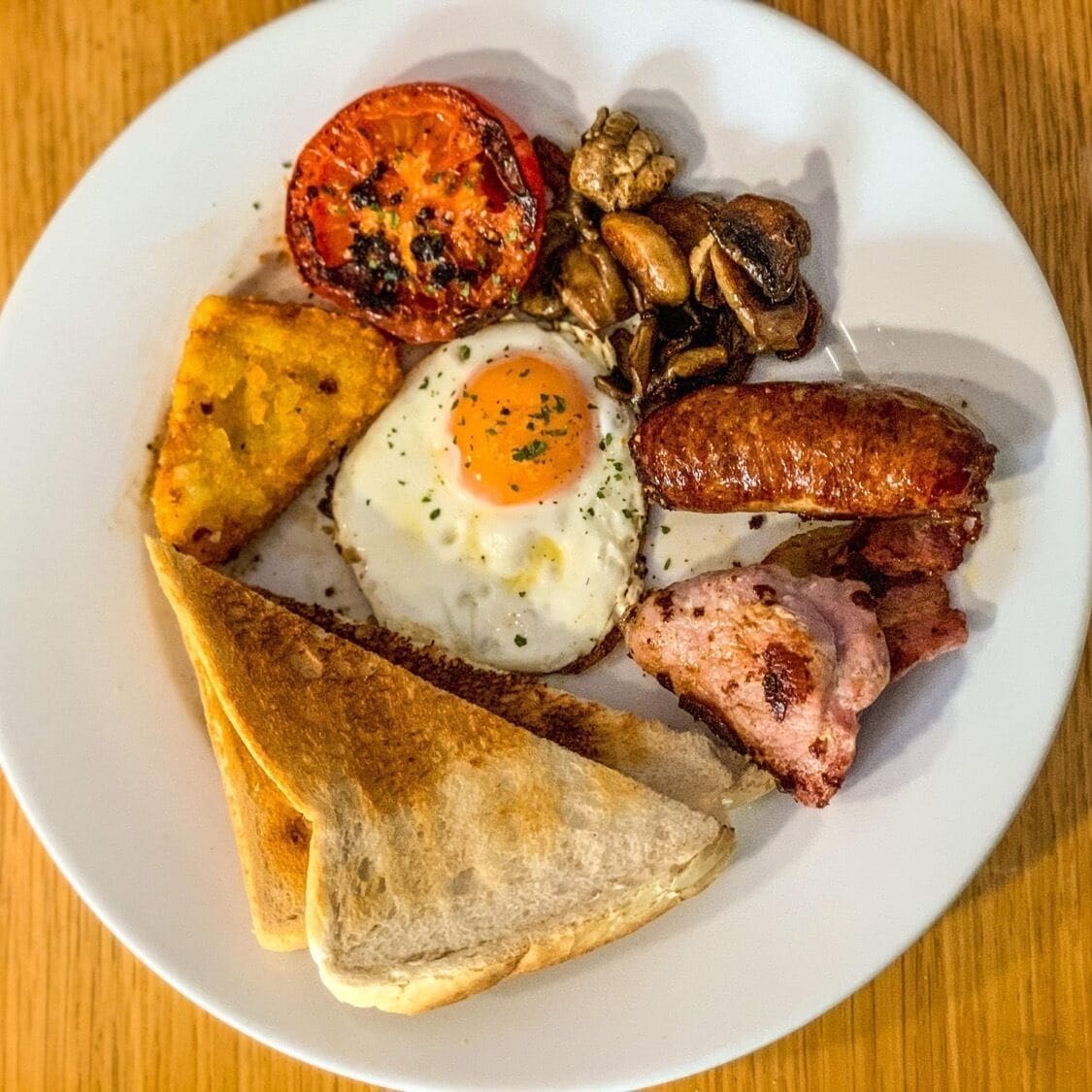 Un plato de comida para el desayuno con huevos, salchichas, tocino, champiñones y tostadas.