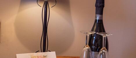 A table with a lamp, a bottle of wine, two wine glasses, and a box of Thorntons Classic chocolates.