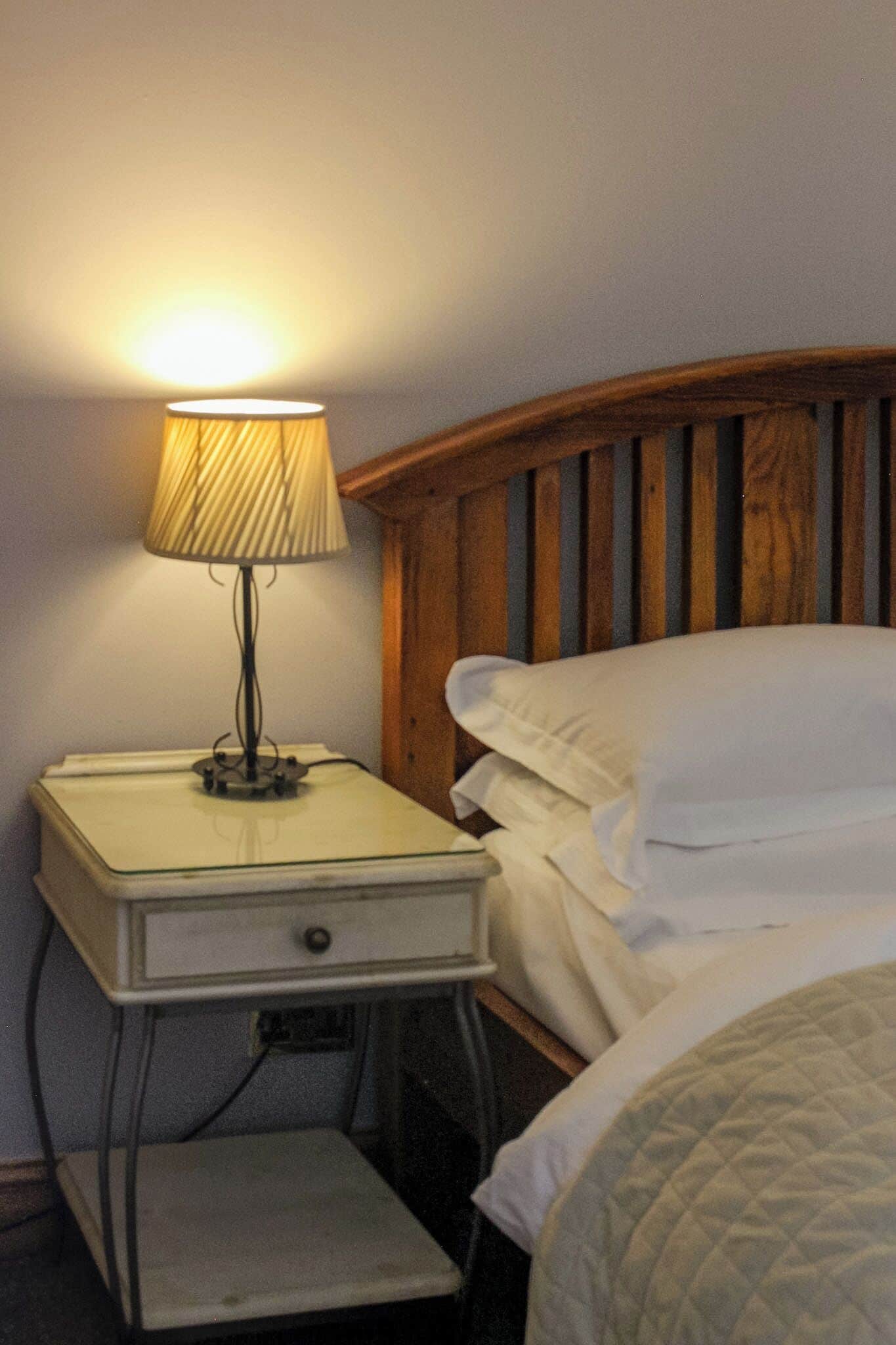 A bed with white bedding, a wooden headboard, and a nightstand with a lamp.