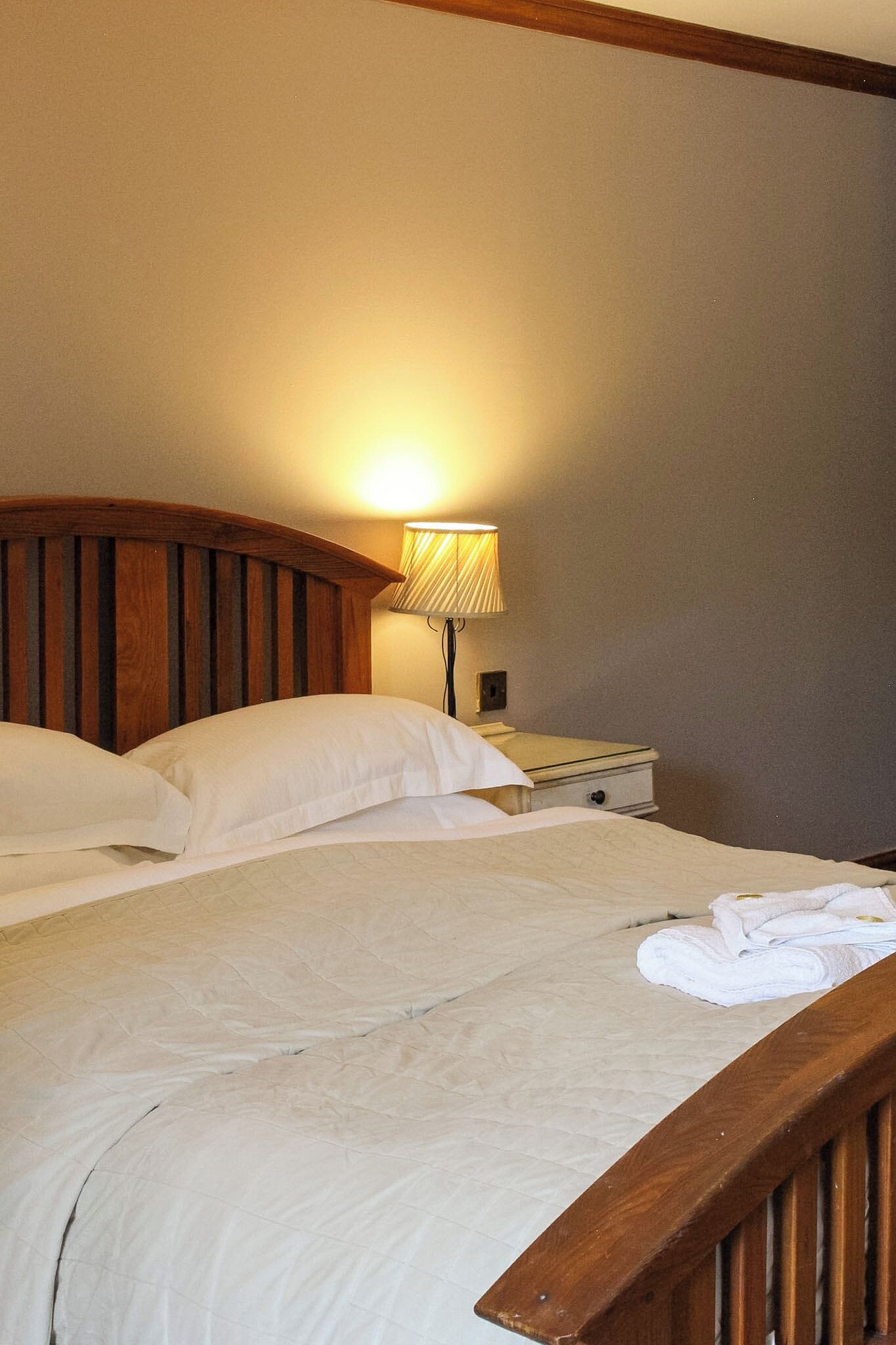 Un lit simple avec une tête de lit en bois, une table de chevet avec une lampe et un lit bien fait, avec une serviette pliée.