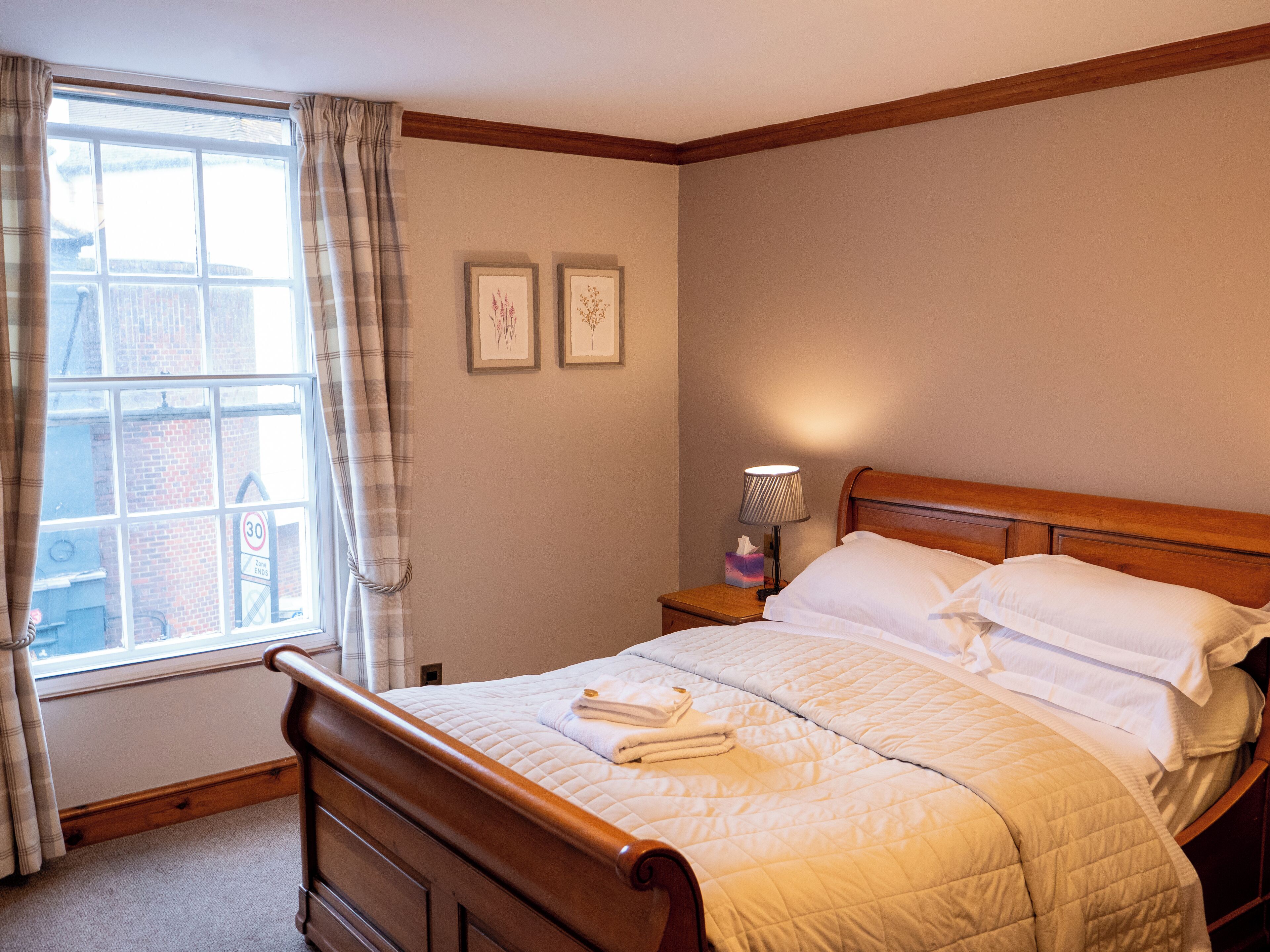 A neatly made bed with white bedding, a wooden headboard, and a bedside table with a lamp and a tissue box.