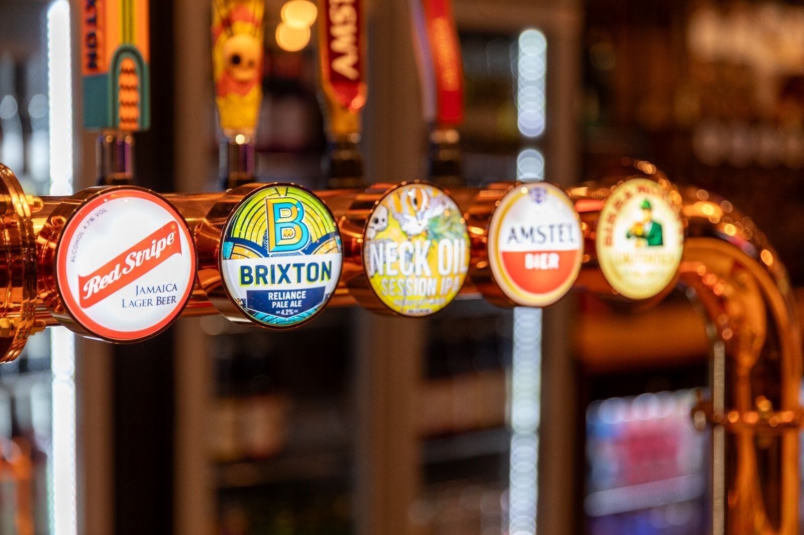 Una hilera de grifos de cerveza con etiquetas para Red Stripe, Brixton, Necks Oil y Amstel.