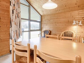 Un intérieur en bois avec une table ronde et des chaises, de grandes fenêtres et un luminaire au plafond.