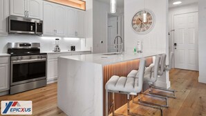 Une cuisine moderne avec des meubles blancs, des appareils en acier inoxydable et un îlot central doté de tabourets de bar.