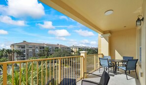 A balcony with a yellow railing, a table with chairs, and a view of multi-story buildings in the background.