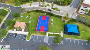 Une vue aérienne d’un parking avec un terrain de basket, un petit bâtiment et une tente bleue.