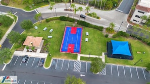 Vista aérea de un estacionamiento con una cancha de baloncesto, un edificio pequeño y una carpa azul.