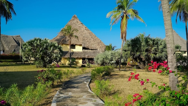 A thatched-roof house with a stone pathway leading to it, surrounded by tropical vegetation and palm trees. - Relaxing Beach Front Villa (Malindi)