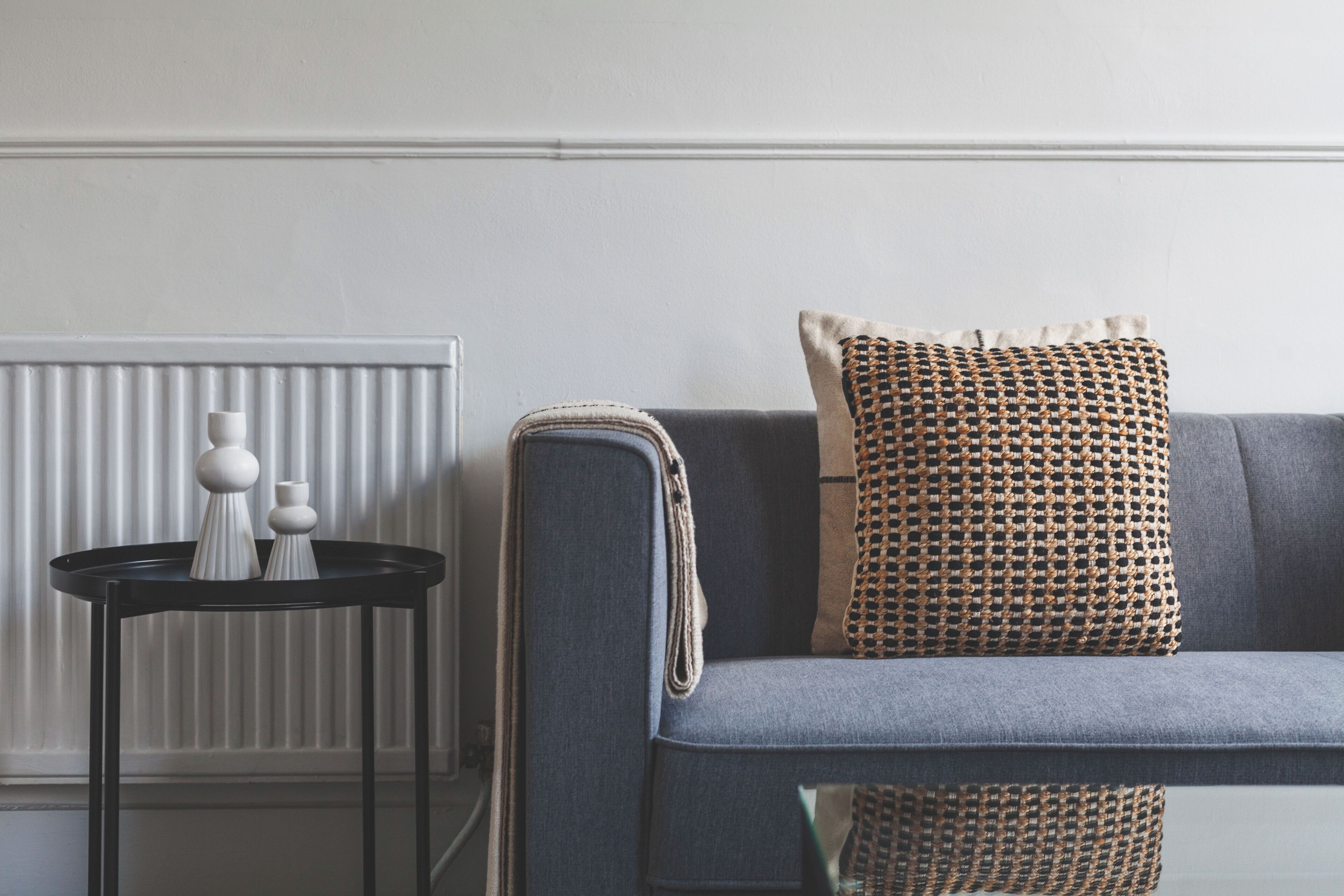 A modern living room with a grey sofa, a woven throw pillow, and a small black side table with white vases.