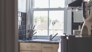 A kitchen with wooden cabinets, a stainless steel refrigerator, and a window with a blind. - The Peckham Luxury Apartment (London)