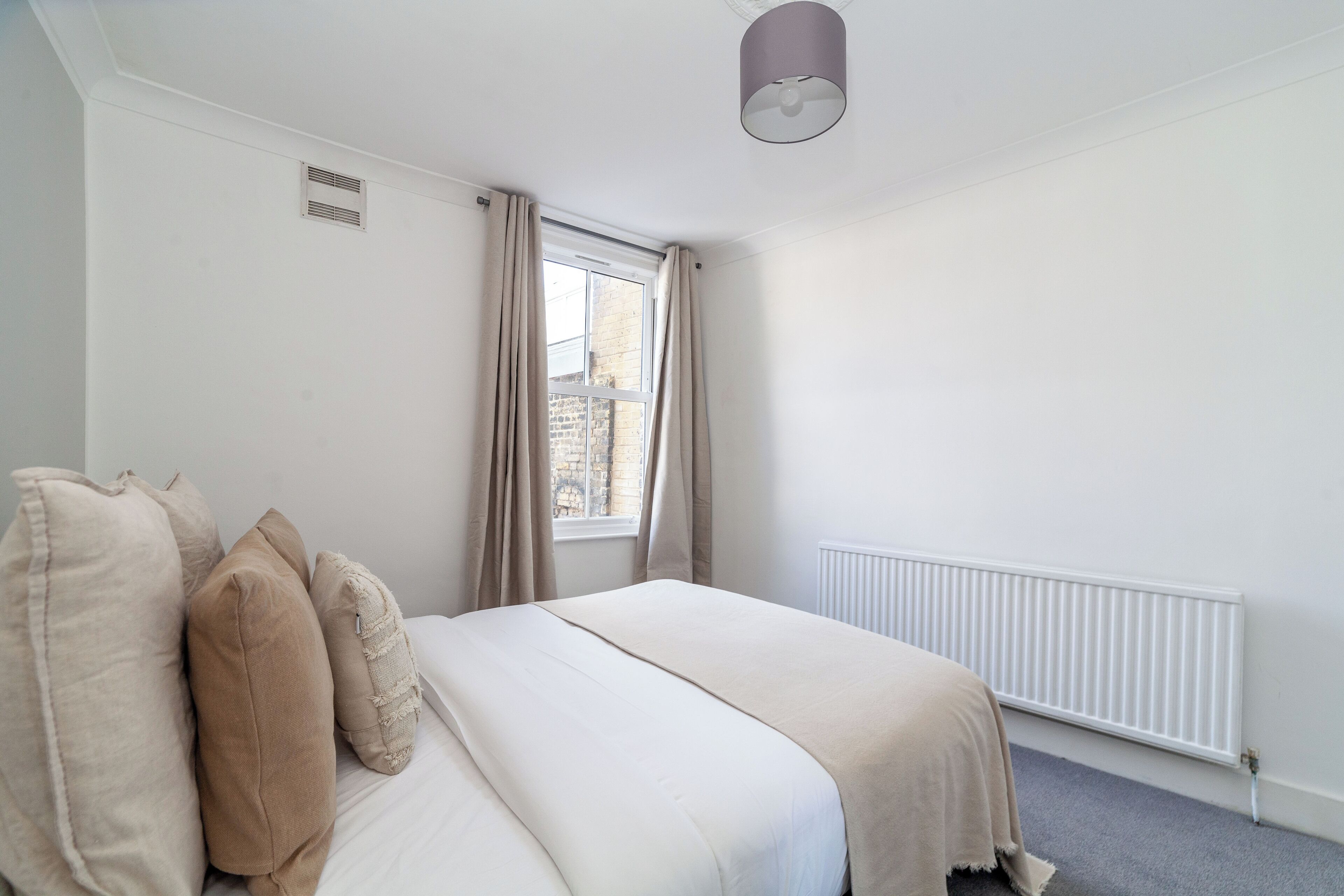 A bedroom with a bed, beige curtains, a window, and a radiator.