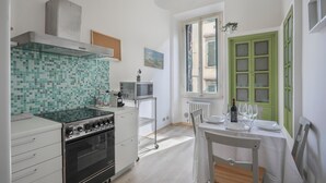 A modern kitchen with a tiled backsplash, stainless steel appliances, a dining area with a table set for two, and a window with green shutters. - Synagogue Suite (Florence)