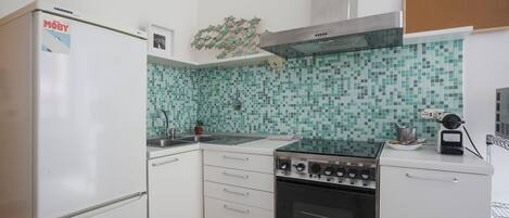 Et lille køkken med hvide skabe, en indbygget ovn og et flisebeklædt backsplash.