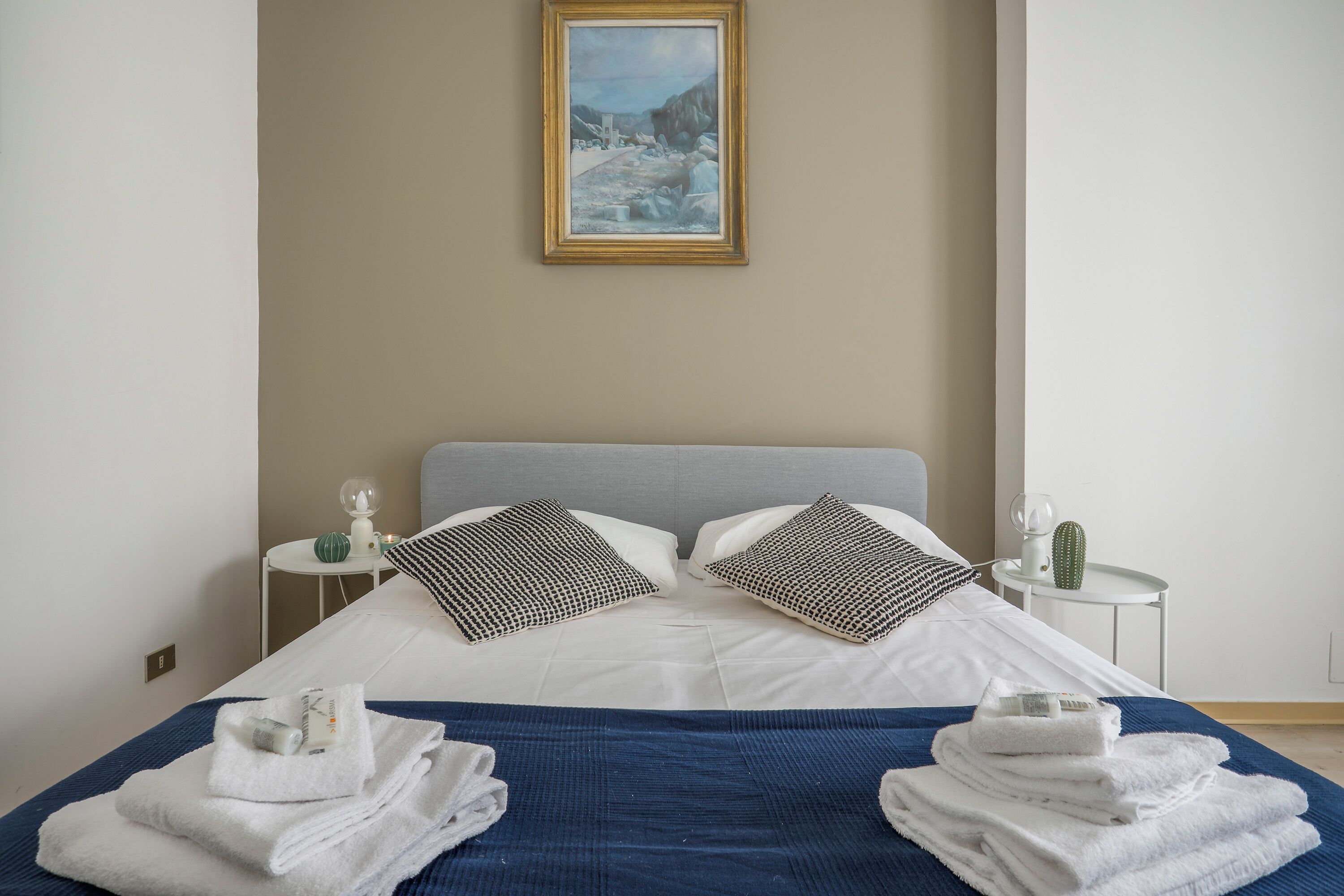 Une chambre d’hôtel avec un lit, des oreillers, un tableau, une petite table avec un cactus et des serviettes.