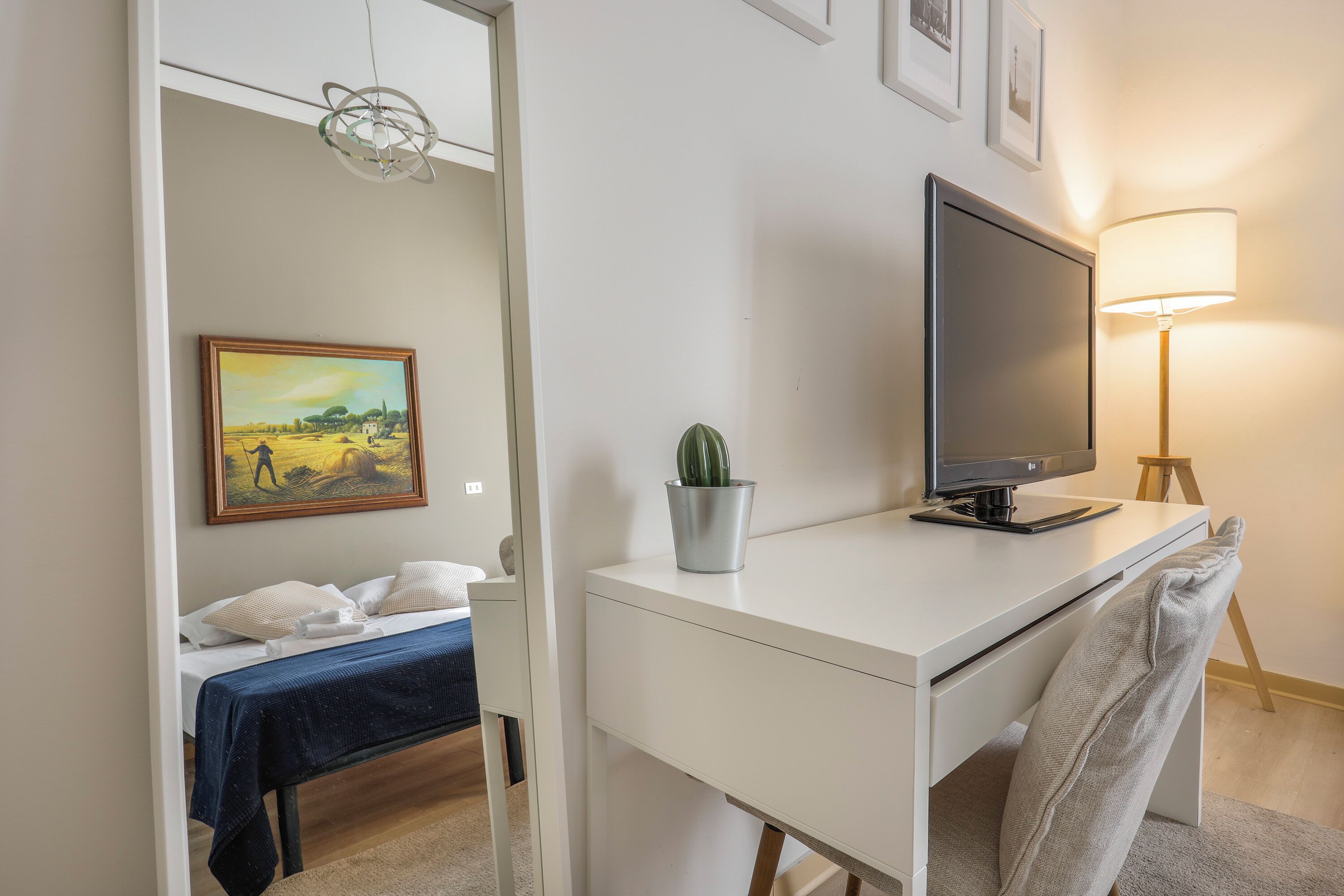 A bedroom with a bed, a desk with a TV, a lamp, and a painting on the wall.