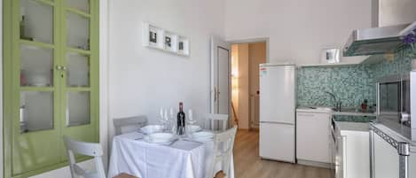 A compact kitchen with a dining area, white cabinetry, and a green-framed door.