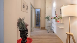 A hallway with a wooden floor, a potted plant, a lamp, and a shelf with a candle. - Synagogue Suite (Florence)