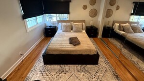 Ein modernes Schlafzimmer mit einem großen Bett, Nachttischen, einem Spiegel und dekorativer Wandkunst.