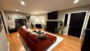Ein Wohnzimmer mit einem roten Sofa, einem Kamin, einem an der Wand befestigten Fernseher und einer schwarzen Tür.