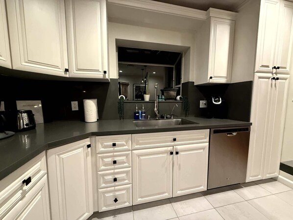 A modern kitchen with white cabinetry, a black countertop, and a built-in dishwasher.