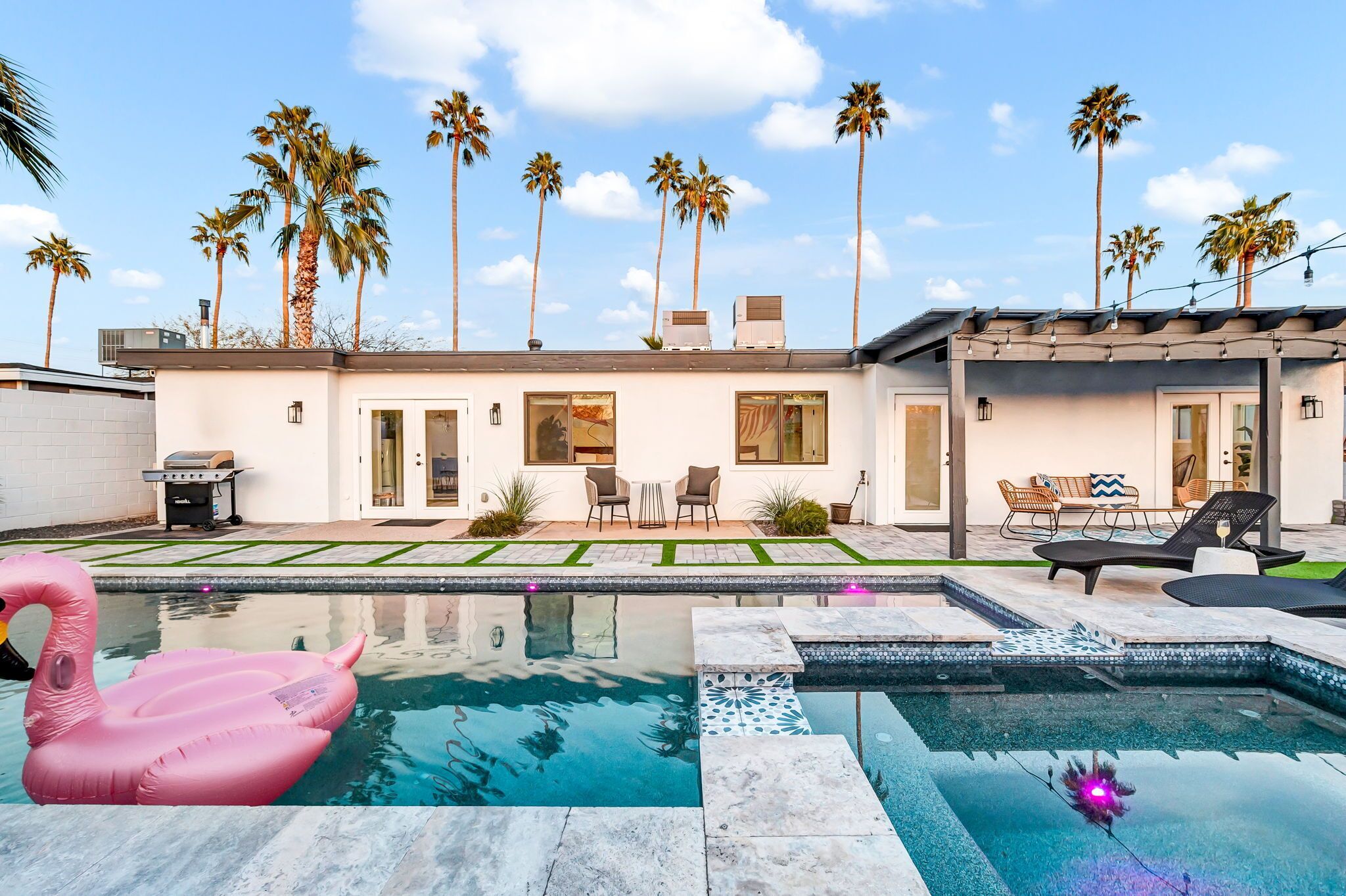 A modern house with a swimming pool, outdoor seating, and palm trees.