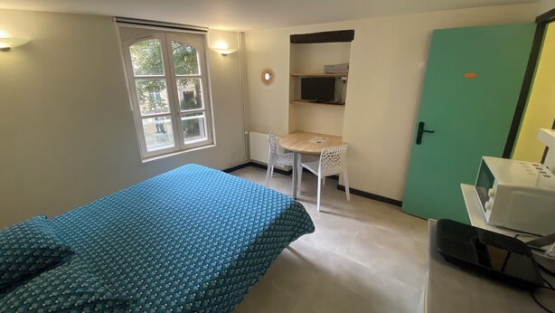 Una habitación con cama, escritorio, silla, computadora y puerta.