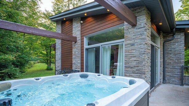 Un bain à remous situé à l’extérieur d’un bâtiment à la façade en pierre et en bois, entouré de verdure.