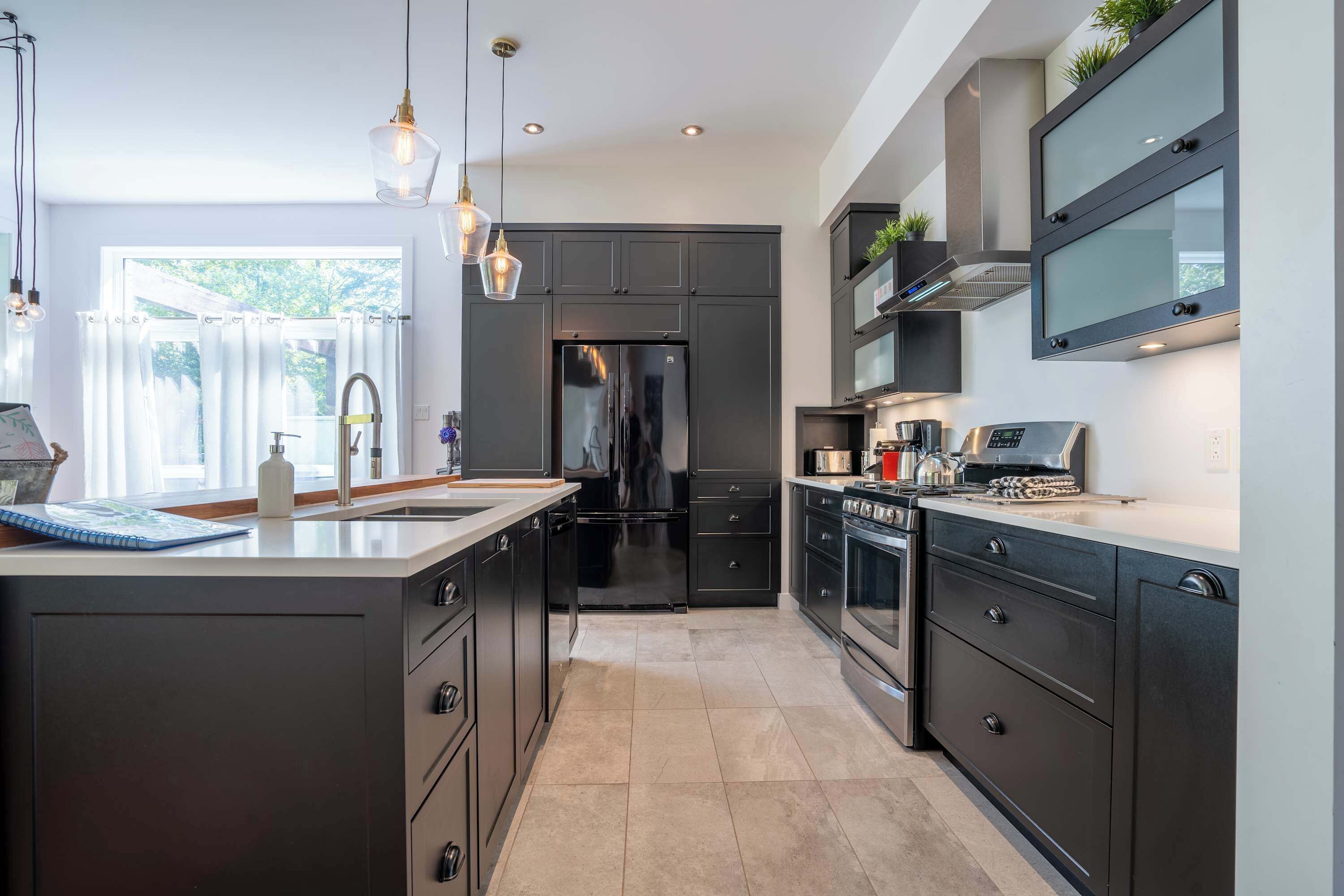 Une cuisine moderne avec des meubles de couleur sombre, des appareils électroménagers en acier inoxydable et des luminaires suspendus.