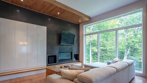 Un salon moderne doté d’une grande fenêtre, d’un téléviseur à écran plat et d’un meuble de rangement intégré pour les appareils multimédias.
