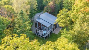 Une cabane entourée d’une forêt dense, dotée d’une terrasse couverte et d’un espace salon extérieur.