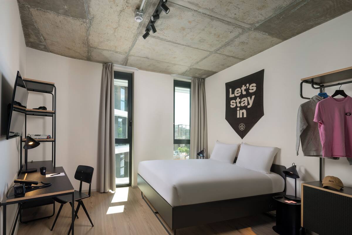 A modern hotel room with a bed, desk, and wardrobe.