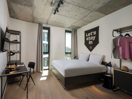 A modern hotel room with a bed, desk, and wardrobe.