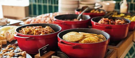 A buffet table with various food items in red pots, including pancakes, waffles, and pies.