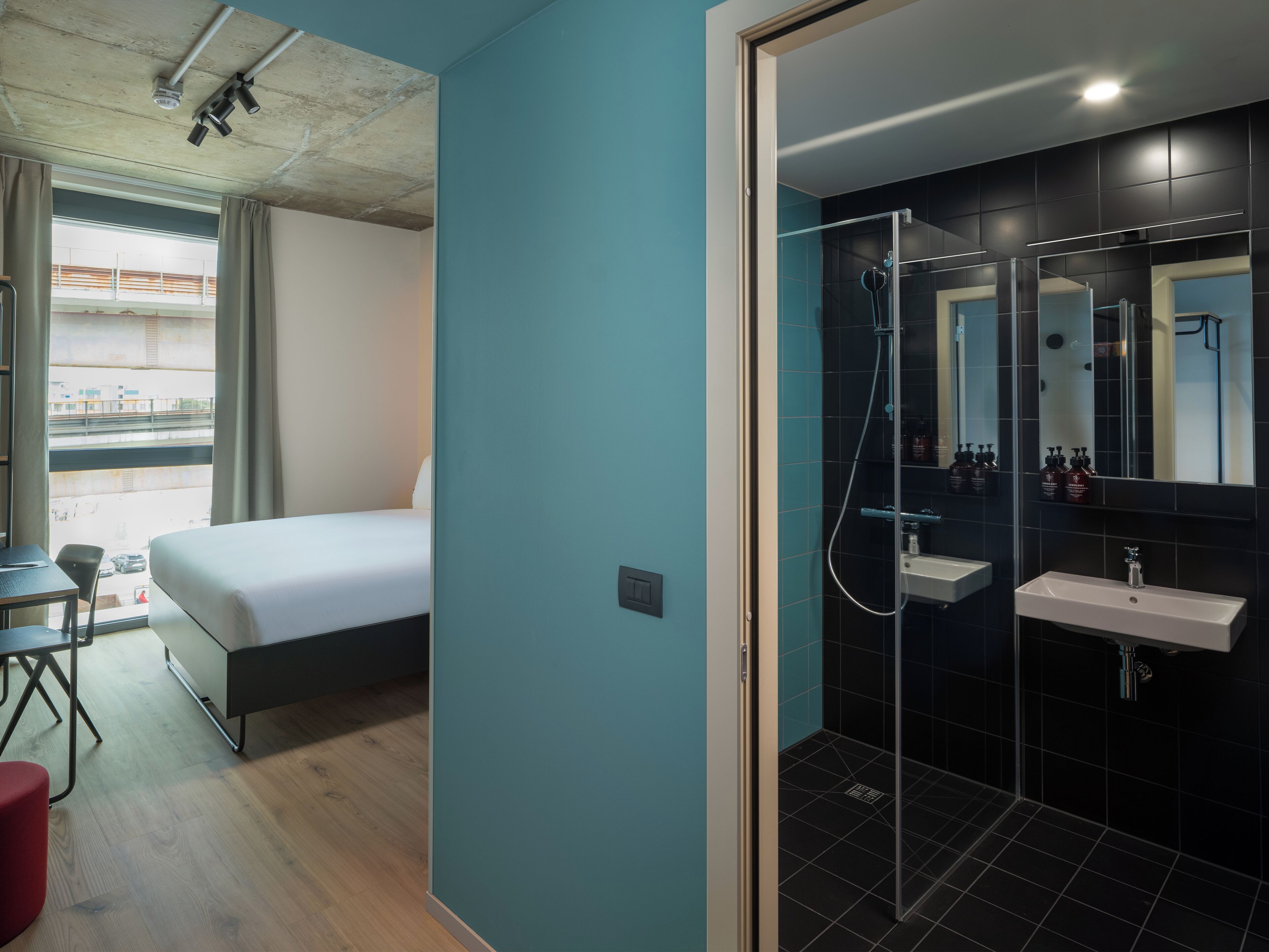 A modern hotel room with a bed, a desk, and a shower area.