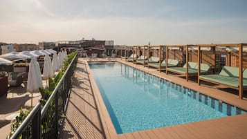 En pool på taget med liggestole og parasoller, omgivet af en træterrasse og metalgelændere.