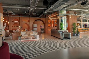 A modern lobby with checkered flooring, a reception desk, seating areas, and exposed ductwork.
