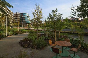 A courtyard with a round wooden table and chairs, surrounded by greenery and trees.