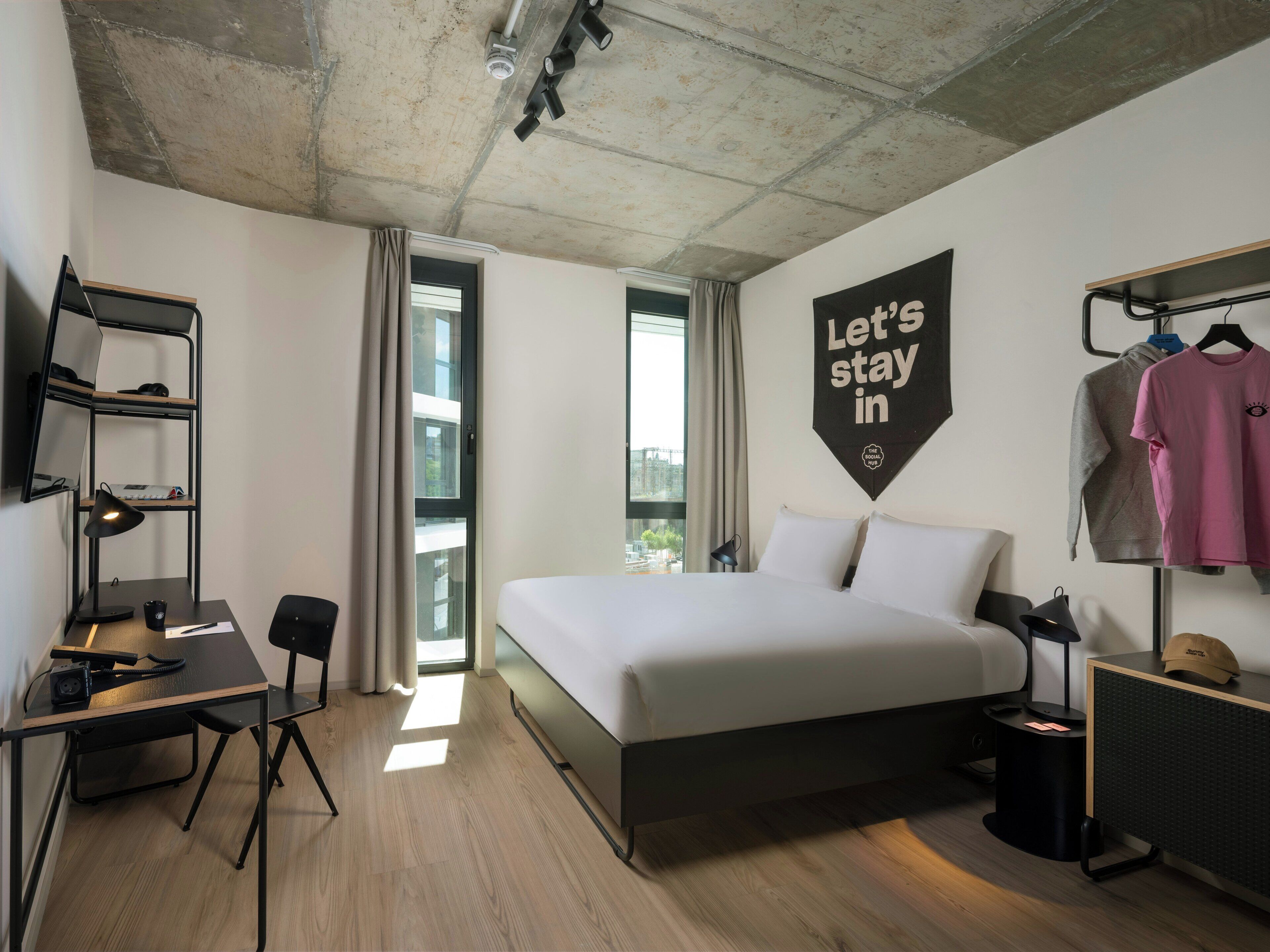 A modern hotel room with a bed, desk, and wardrobe.