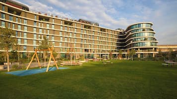 Un hotel moderno con fachada de vidrio curva, un patio con césped y un columpio, y un jardín bien cuidado.