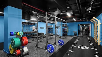 Une salle de sport équipée de matériel de musculation, avec un mur bleu et un sol noir marqué de lignes blanches.