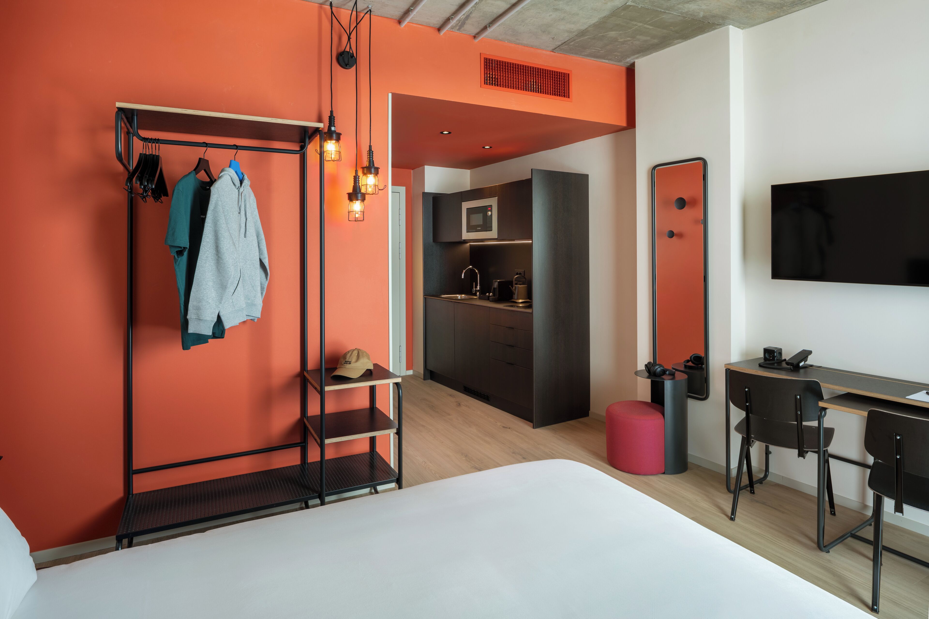 Een moderne hotelkamer met een bed, een bureau, een stoel, een garderobe en een kitchenette.
