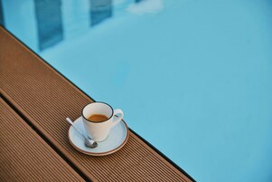 Eine Kaffeetasse auf einem Holztisch am Pool.