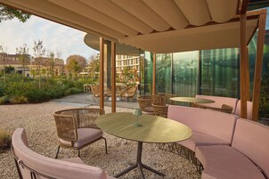 An outdoor seating area with wicker furniture and a glass wall providing a view of the cityscape.