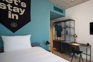 A modern hotel room with a bed, a desk, a chair, a wardrobe, and a hanging sign.